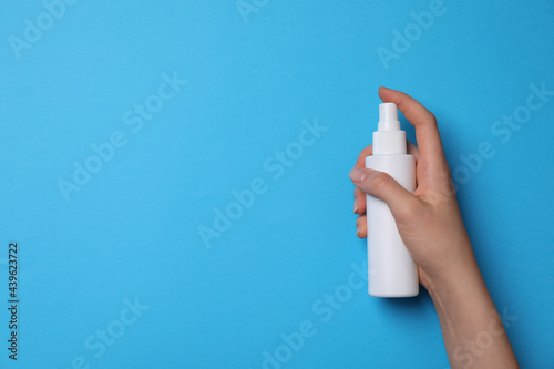Woman holding hand sanitizer on light blue background, closeup view with space for text. Safety equipment