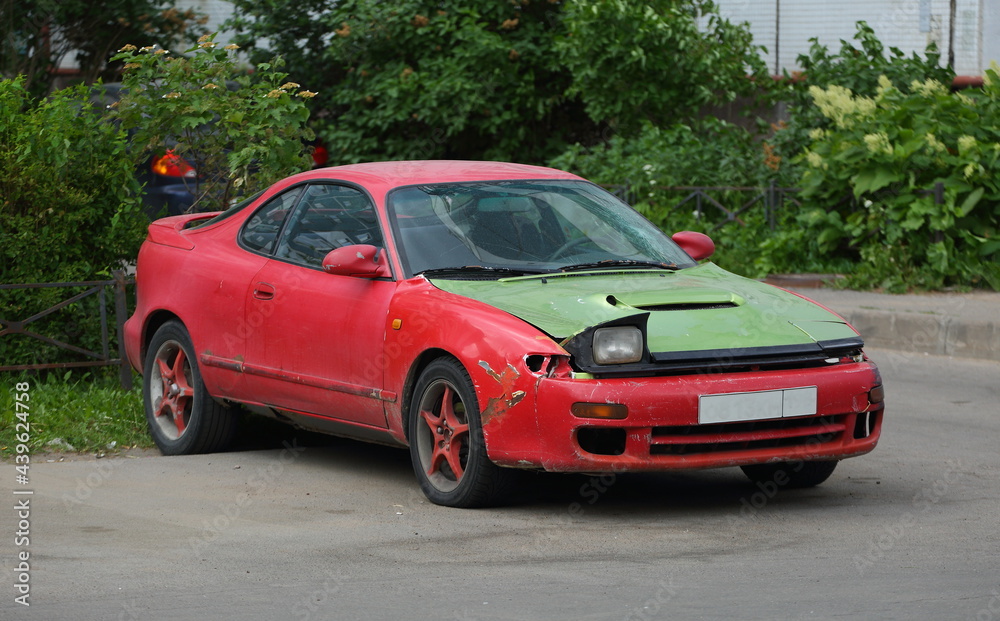 An old broken down red sports car with a green hood, Iskrovsky Prospekt, Saint Petersburg, Russia, June 2021