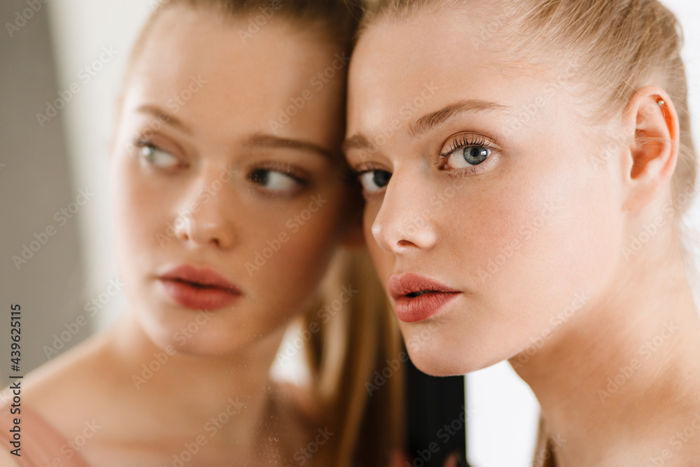 Young blonde white woman looking at camera while standing by mirror
