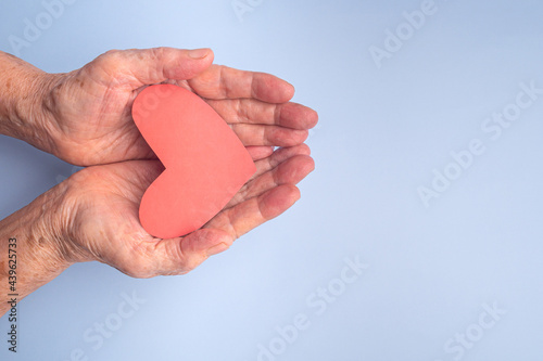 People  age  love  and health care concept. Red paper cut a heart shape on the palm of a senior woman with a blue background. Healthcare  wellbeing  World heart day  World health day. Valentine s day