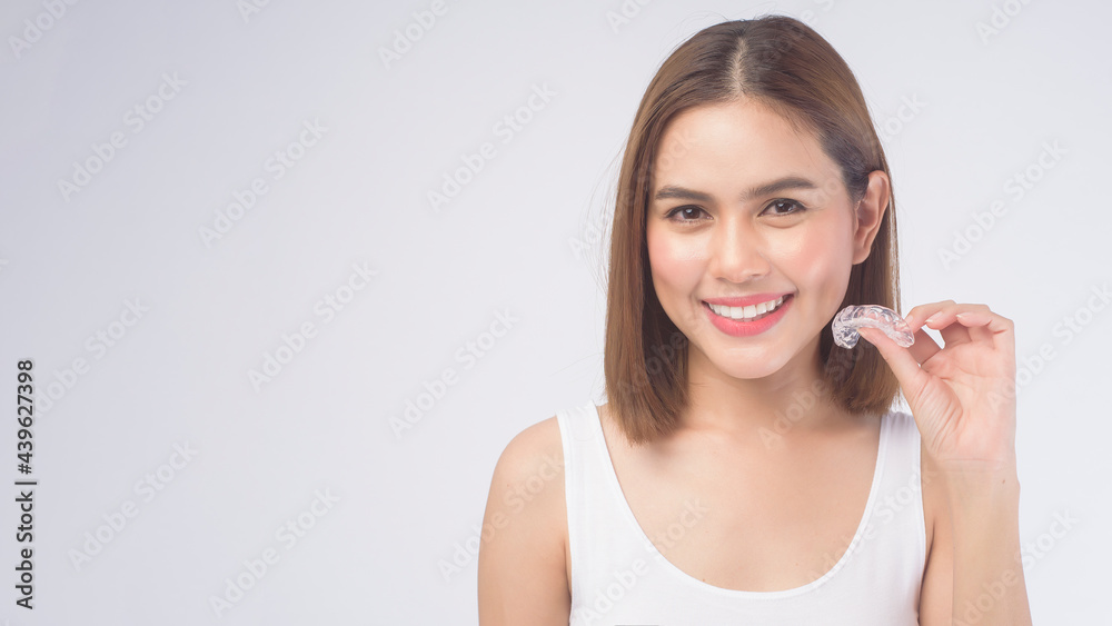 Young smiling woman holding invisalign braces over white background studio, dental healthcare and Orthodontic concept. Young smiling woman holding invisalign braces over white background studio, dental healthcare and Orthodontic concept.