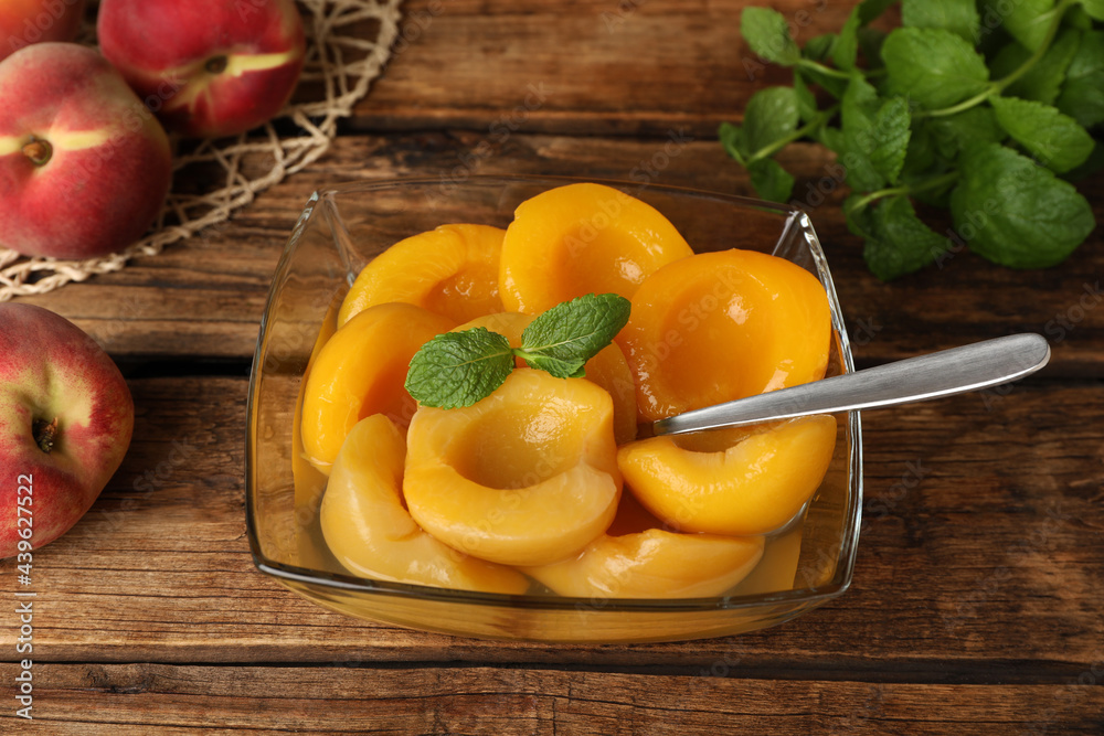 Canned peach halves in bowl on wooden table