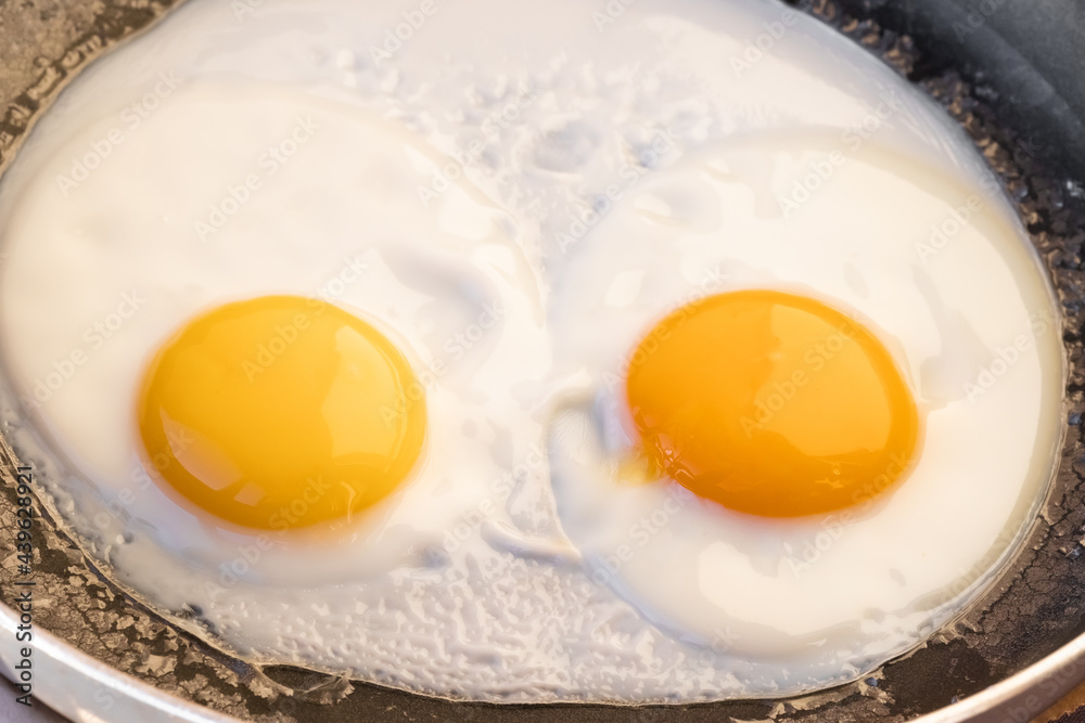 Cooked fried eggs with two bright round raw yolks in a black skillet. Simple breakfast option. Top view, close-up. Look like eyes Cooked fried eggs with two bright round raw yolks in a black skillet. Simple breakfast option. Top view, close-up. Look like eyes
