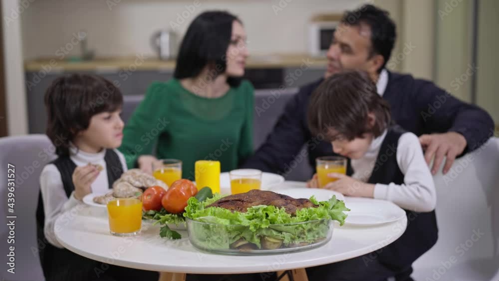 Dinner table with blurred family eating food at background talking smiling. Positive Caucasian woman Middle Eastern man and twin brothers at home in the evening. Family Dinner table with blurred family eating food at background talking smiling. Positive Caucasian woman Middle Eastern man and twin brothers at home in the evening. Family