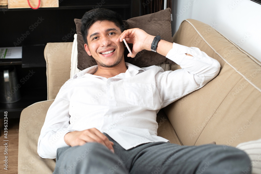 Obraz premium Latino man talking on the mobile phone lying on the sofa at home