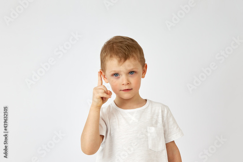 Portrait of a boy with a confident face in a white T shirt pointing up on a white background