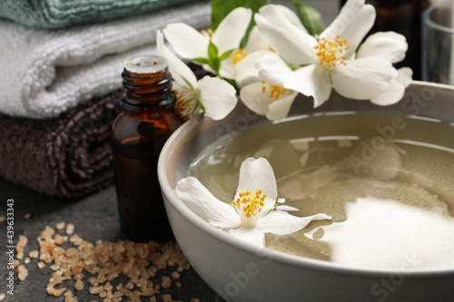 Beautiful spa composition with jasmine essential oil and fresh flowers on grey table  closeup
