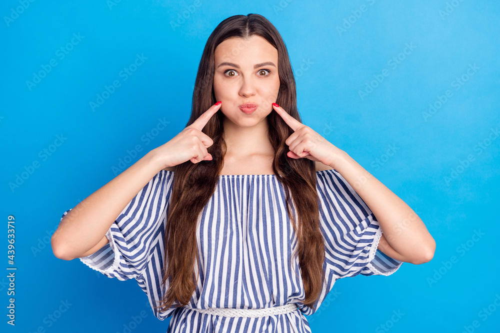 Photo of childish funny young woman dressed striped outfit press fingers bloated cheeks isolated blue color background Photo of childish funny young woman dressed striped outfit press fingers bloated cheeks isolated blue color background