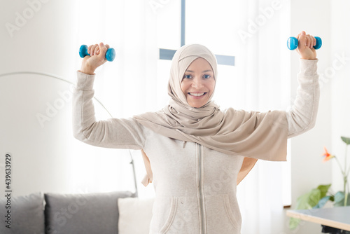Healthy strong arabian muslim islamic female in hijab training with dumbbells at home. Workout fitness on lockdown concept