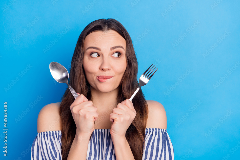 Photo portrait woman hungry wait for dinner with fork knife biting lip looking copyspace isolated bright blue color background Photo portrait woman hungry wait for dinner with fork knife biting lip looking copyspace isolated bright blue color background