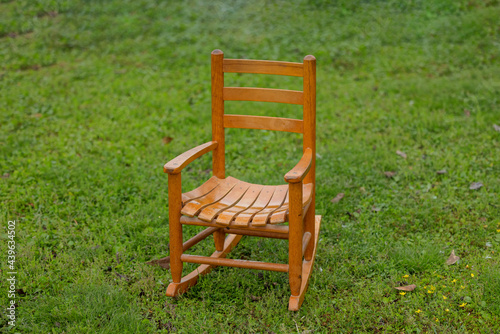 a small wood wooden child's rocking chair sitting outside alone on the grass