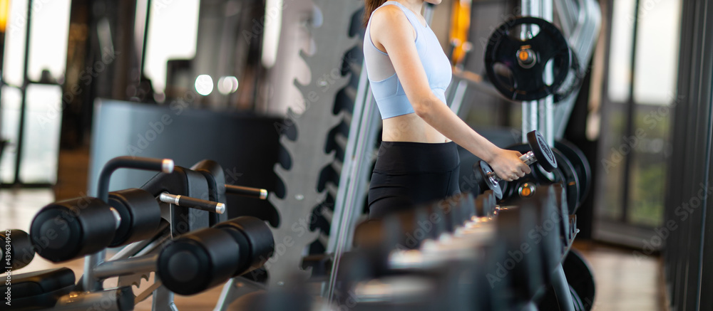 Fototapeta premium Side view of Woman lifting dumbbell weights getting ready for exercise in fitness