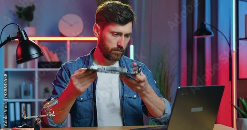 Likable concentred experienced bearded man attantivly considering computer panel in his hands and searching instructions of its working in internet photo