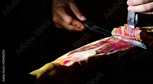 Gastronomía y alimentación en España. Detalle de primer plano de maestro cortador de jamón ibérico sobre fondo oscuro. photo