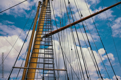 sailing mast with ropes in front of cloudy blue sky