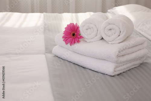 Fresh white towels with flower on bed indoors, space for text