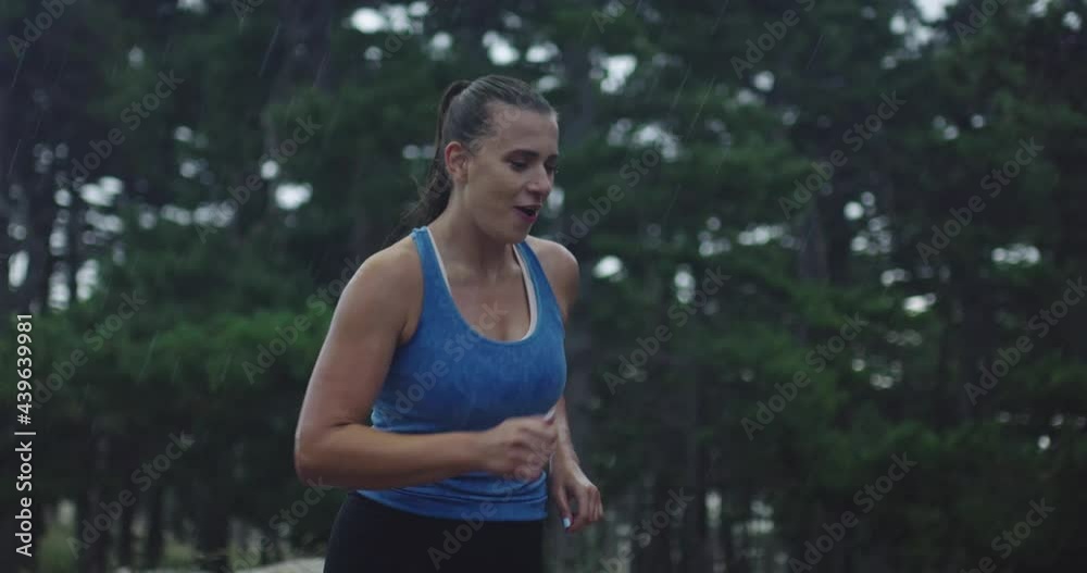 Slow motion tracking shot of a young woman in sportswear jogging through an evergreen forest on a country road on heavy rain. Slow motion tracking shot of a young woman in sportswear jogging through an evergreen forest on a country road on heavy rain.