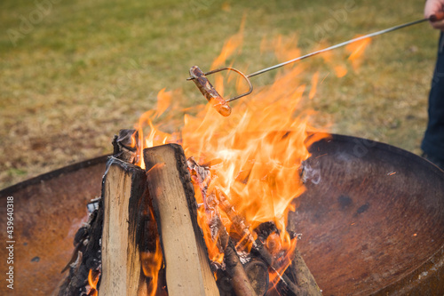 Mann grillt Nürnberger Bratwurst am Spieß über Lagerfeuer Holz Feuer einer Metall Feuerschale im Garten photo