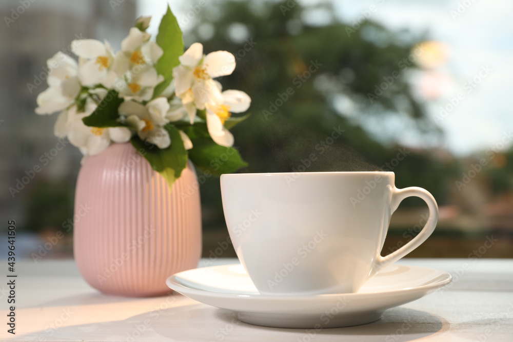 Cup of delicious morning coffee and vase with flowers on table outdoors