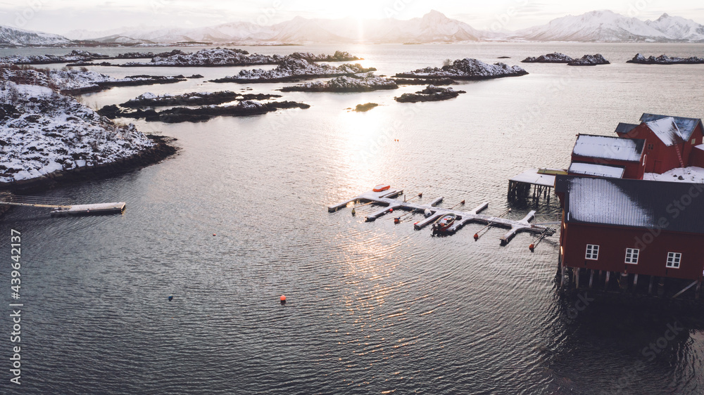 Breathtaking bird's eye view of Lofoten archipelago covered with snow surrounded by Norway sea water. Aerial view from drone of small fishing bay with pier at golden sunset light