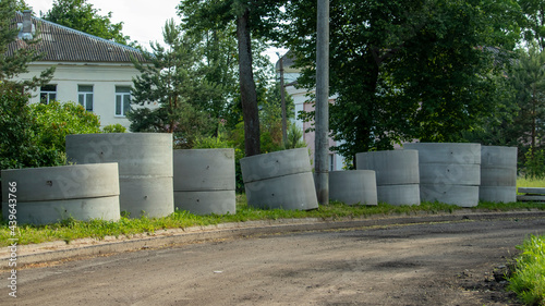 reinforced concrete rings from manholes lie on the grass by the road © Mihail