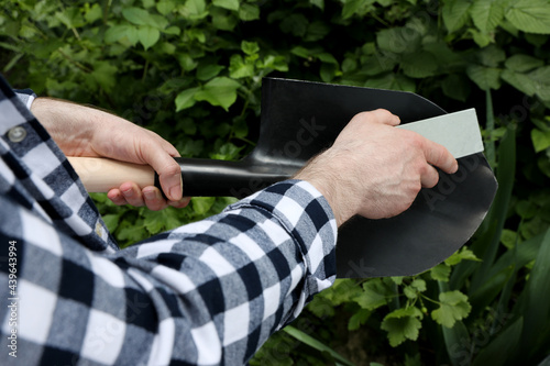 Man sharpening shovel outdoors, closeup. Gardening tools