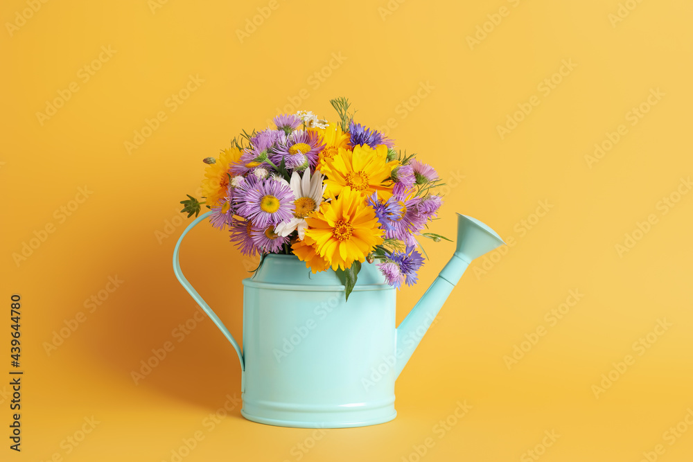 Light blue watering can with beautiful flowers on yellow background