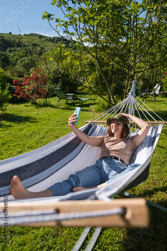 Woman lying in hammock taking a photo of herself having a good time in the garden.