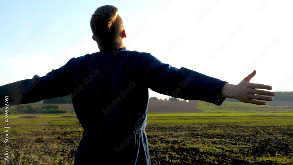 Fototapeta premium A farmer walks across a field of ripe wheat in rays of the sunset. Agricultural plantation. A businessman examines his wheat field, analysis of the grain harvest. Ears with grain in a field in the sun