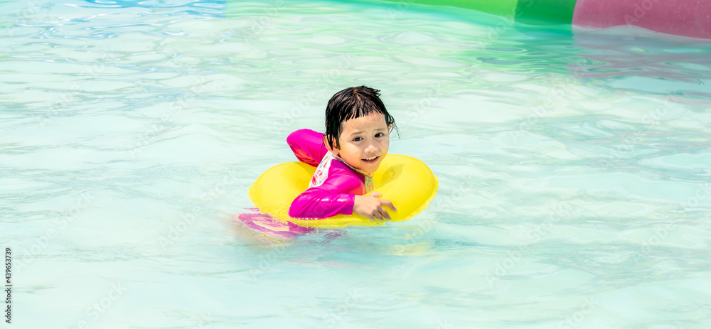 Happy young little kid girl with a yellow inflatable ring at the outdoor swimming pool on summer sunny day