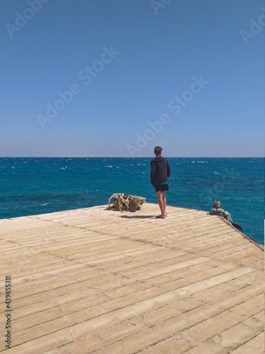 Young man standing alone on edge of footbridge and staring at sea