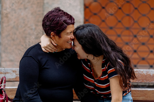Mother and daughter hugging while are sitting on an urban bench  photo