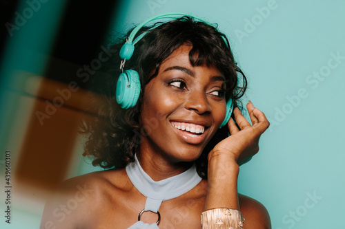 Happy young black woman listening to music over blue background photo