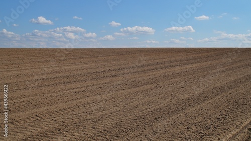 brown plowed farmland under the blue sky with white clouds 