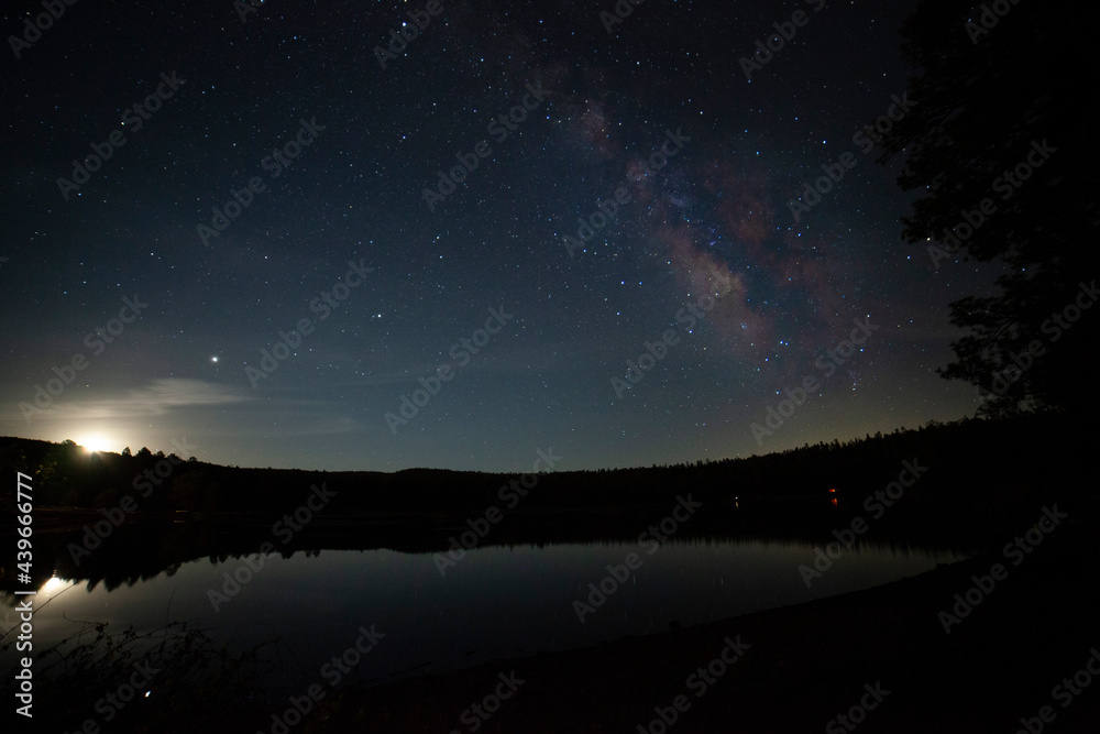 Rising moon and Milky Way stars over a calm lake in the forest Rising moon and Milky Way stars over a calm lake in the forest