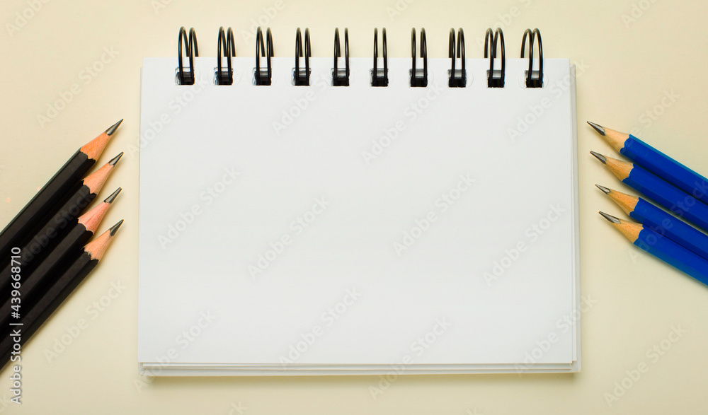 On a light background, a white notebook with a place to insert text or illustrations and black and blue pencils on the side. Template On a light background, a white notebook with a place to insert text or illustrations and black and blue pencils on the side. Template