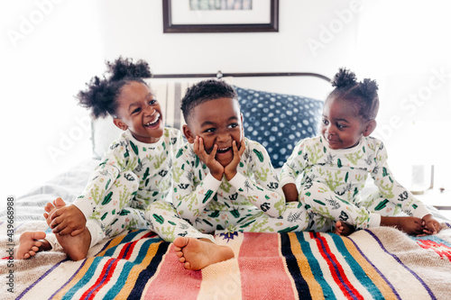 Three siblings in matching pajamas sitting on the bed. 