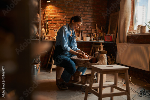 Beautiful young Caucasian female artisan working with fresh wet clay in pottery workshop