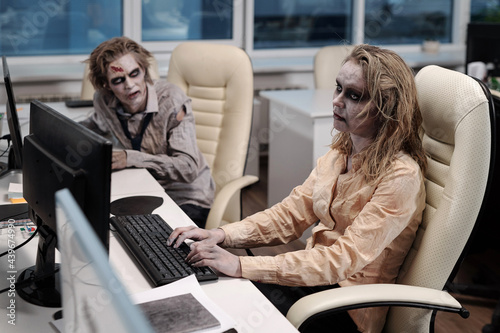 Gloomy businesswoman with zombie greesepaint using computer by desk