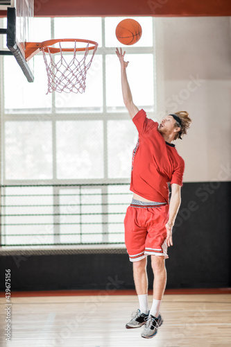 Ginger man in a red sportswear throwing the ball to the basket
