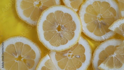 Citrus lemon slices on yellow background moving in water with ripples