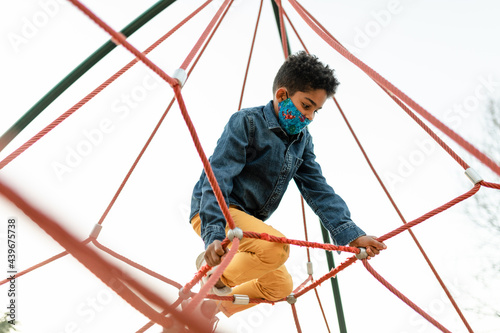 Child Wearing a Mask Enjoys Climbing While at the Park photo