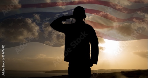 Composition of silhouette of saluting soldier against sunset sky with billowing american flag