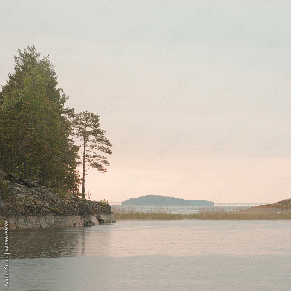 Sunrise on Lake Ladoga with light fog. Calm on the lake. Island with pine trees.