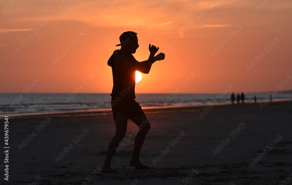 A fighter training on the beach at sunset