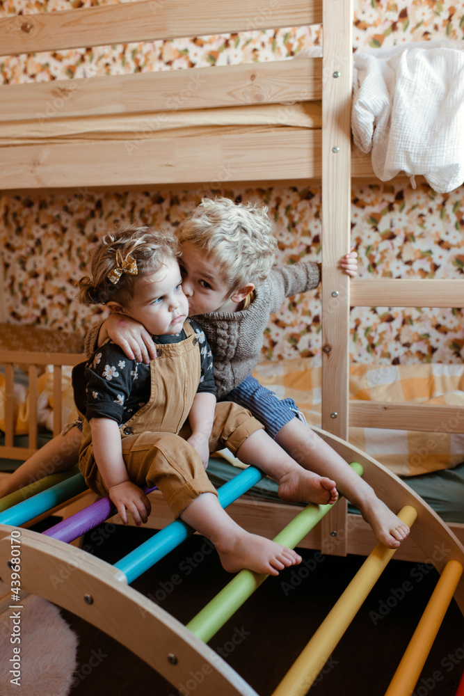 Brother and sister sitting on a rainbow pikler in their bedroom Brother and sister sitting on a rainbow pikler in their bedroom