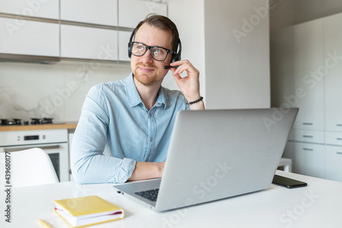 Smiling young male freelancer wearing a headset and looking away, a positive man with the beard working remotely in the customer service department, making and receiving calls