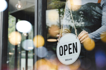 hand of asain staff woman wearing apron turning open sign board on glass door in modern cafe coffee shop, hotel service, cafe restaurant, retail store, small business owner, food and drink concept
