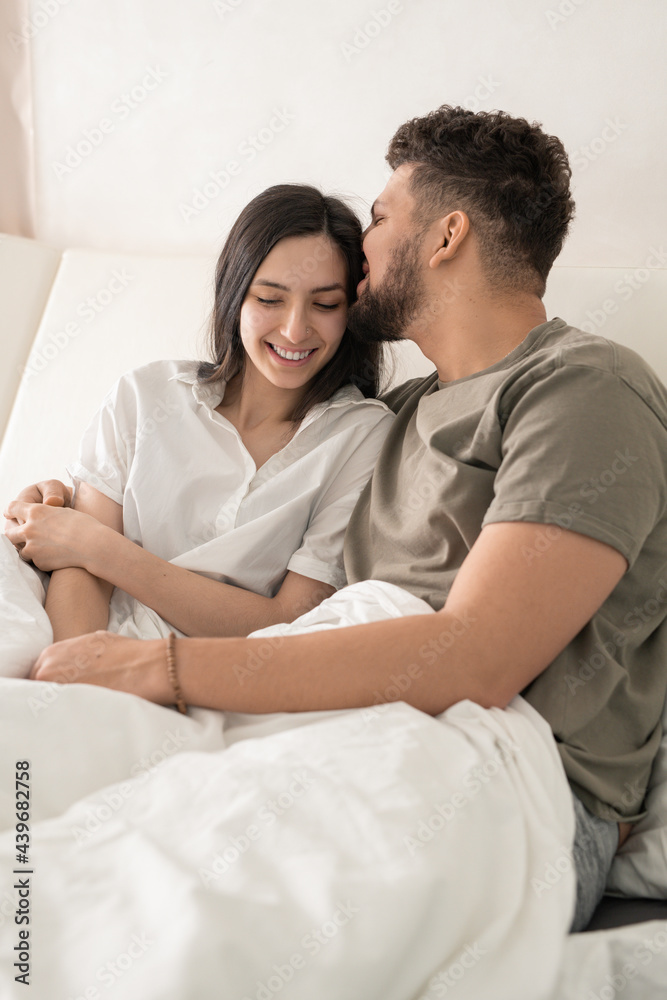 Happy young man kissing his smiling wife in bed Happy young man kissing his smiling wife in bed