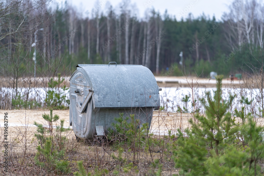 the waste container is located at the water tank on the shore between small trees and grass. the waste container is located at the water tank on the shore between small trees and grass.